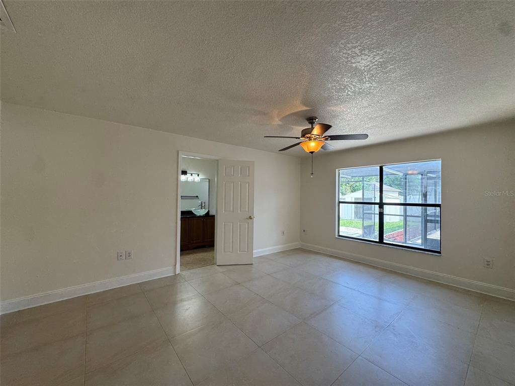 A bedroom with tile flooring, a ceiling fan, and a doorway leading to a bathroom — 14 YORK COURT, KISSIMMEE, FL
