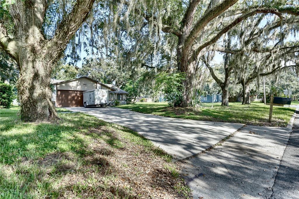 A concrete driveway leads to a house with a garage and a trailer under large trees — 101 N ELLIOTT AVENUE, SANFORD, FL