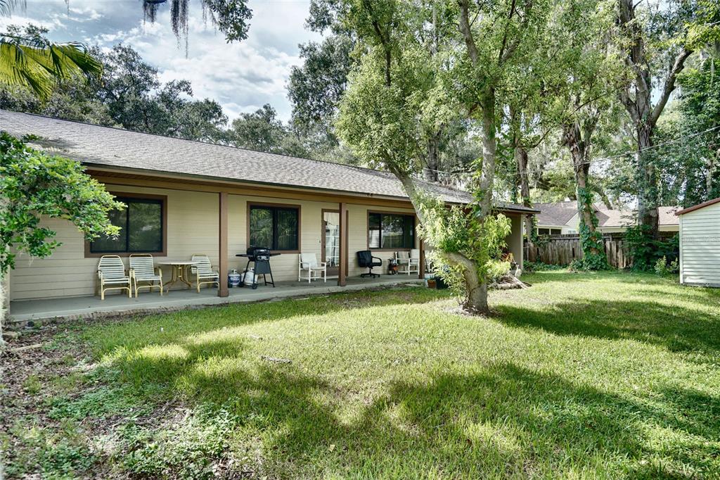 A single-story house with a covered porch, outdoor seating, and a grassy backyard with trees — 101 N ELLIOTT AVENUE, SANFORD, FL