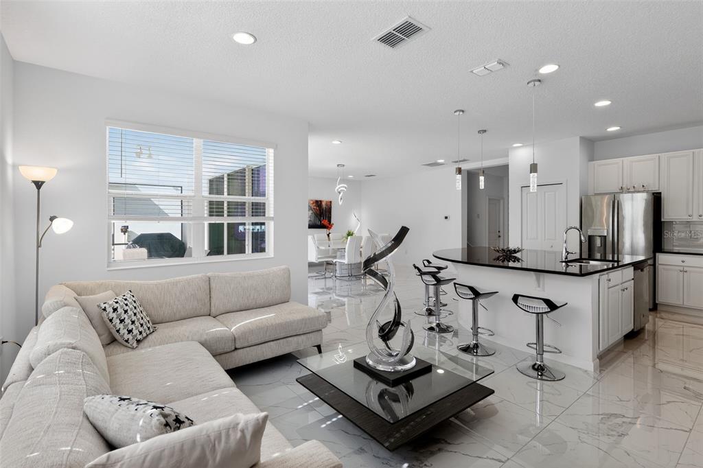 An open-concept living room and kitchen featuring white cabinetry, marble-look tile floors, and modern furniture — 4577 CABELLO LOOP, KISSIMMEE, FL