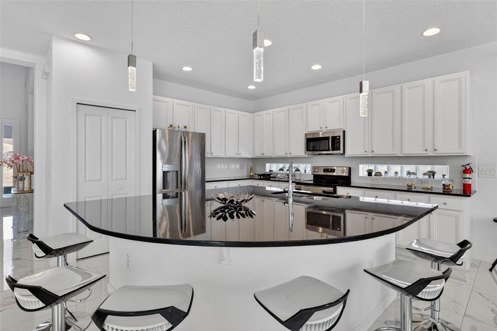 A modern kitchen features white cabinetry, black countertops, a curved island, and stainless steel appliances — 4577 CABELLO LOOP, KISSIMMEE, FL