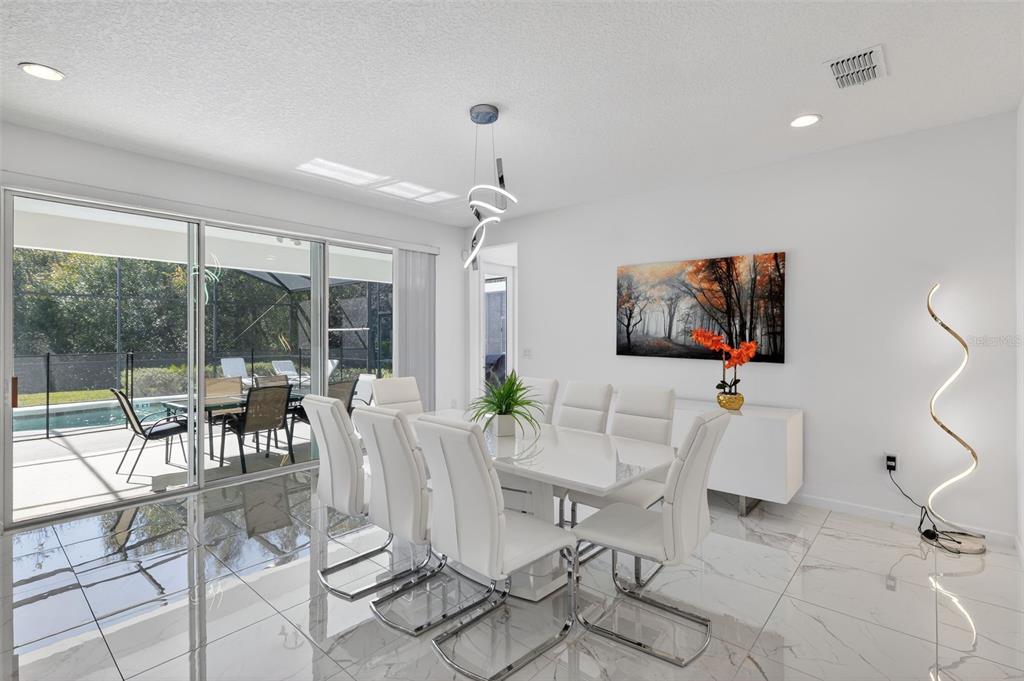 A modern dining room features white furniture, marble-look tile floors, and a sliding glass door — 4577 CABELLO LOOP, KISSIMMEE, FL