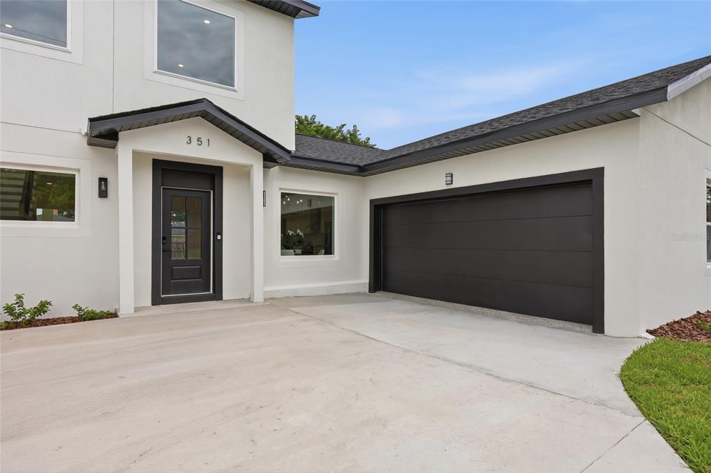 The exterior of a modern two-story house features white stucco walls, a black garage door, and a front entrance — 351 E WILDMERE AVENUE, LONGWOOD, FL