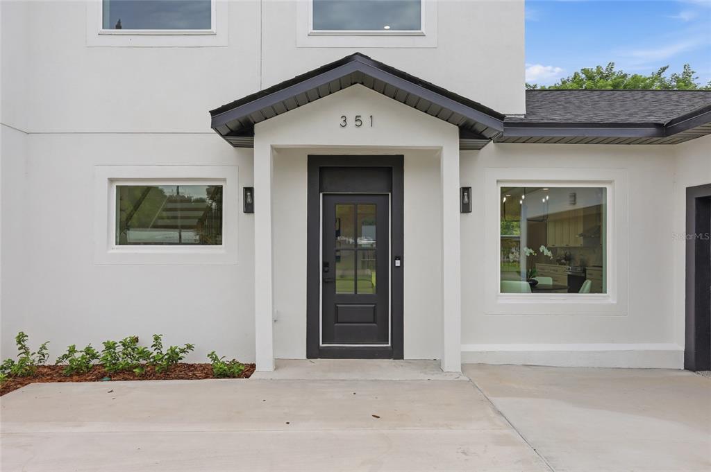 The exterior of a white house features a dark-framed front door and large windows — 351 E WILDMERE AVENUE, LONGWOOD, FL