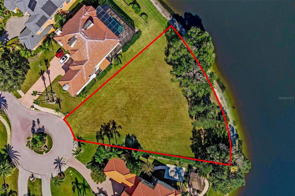 An aerial view shows a vacant, triangular waterfront lot outlined in red between two houses — 17903 BIMINI ISLE COURT, TAMPA, FL