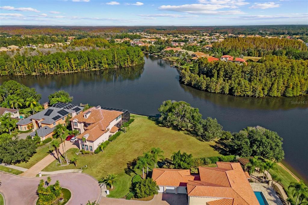 An aerial view shows two large houses with terracotta roofs situated beside a winding lake — 17903 BIMINI ISLE COURT, TAMPA, FL