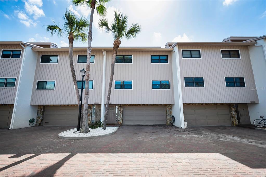 A three-story townhouse exterior features vertical siding, multiple windows, and three attached garages — 12334 CAPRI CIRCLE N, TREASURE ISLAND, FL