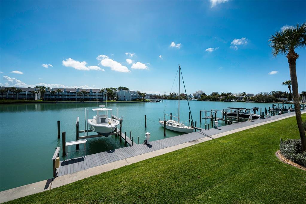 A grassy lawn overlooks a canal with a boat lift, a sailboat, and several docks — 12334 CAPRI CIRCLE N, TREASURE ISLAND, FL