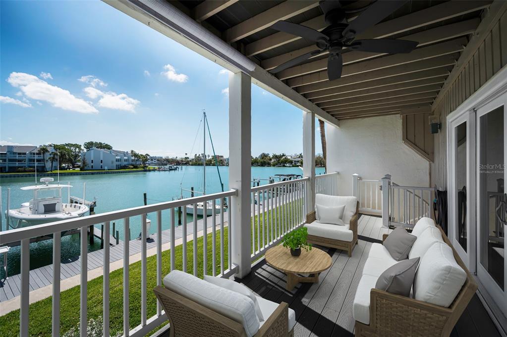 A covered balcony with outdoor furniture overlooks a canal with boats and a dock — 12334 CAPRI CIRCLE N, TREASURE ISLAND, FL