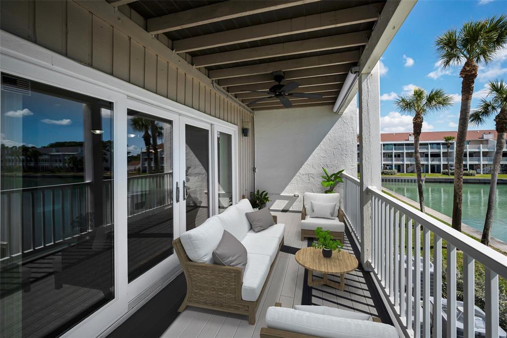 A furnished balcony features a white sofa, chairs, and a round table overlooking a canal — 12334 CAPRI CIRCLE N, TREASURE ISLAND, FL