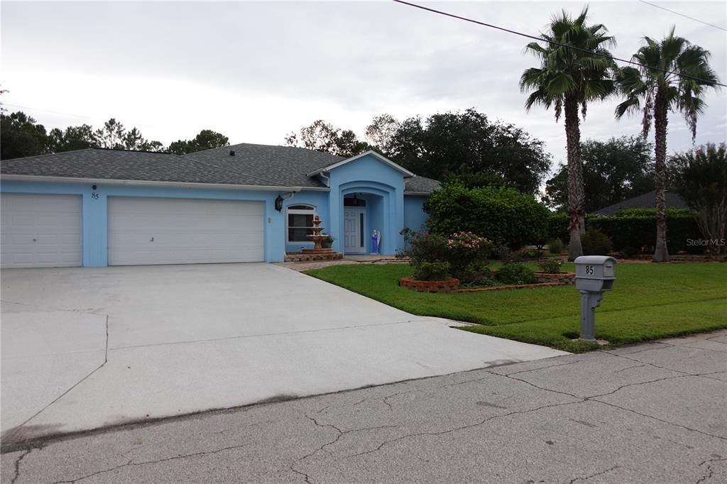 A light blue single-story house features a two-car garage, a front fountain, and palm trees — 85 LANCELOT DRIVE, PALM COAST, FL