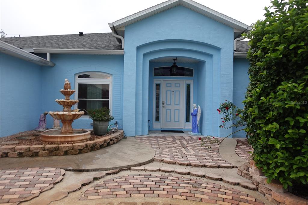 A light blue house exterior features a brick walkway, a tiered fountain, and an angel statue — 85 LANCELOT DRIVE, PALM COAST, FL