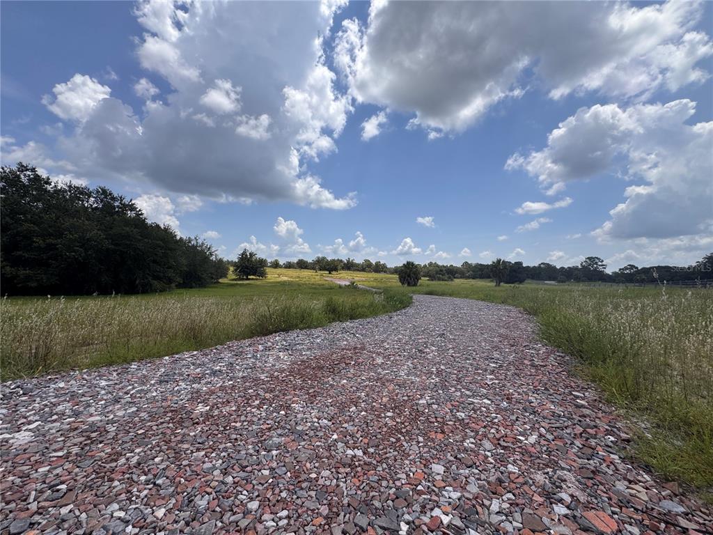 A gravel driveway leads through a grassy field under a bright, cloudy sky — 4557 GLEN SAINT MARY ROAD, LAKE WALES, FL