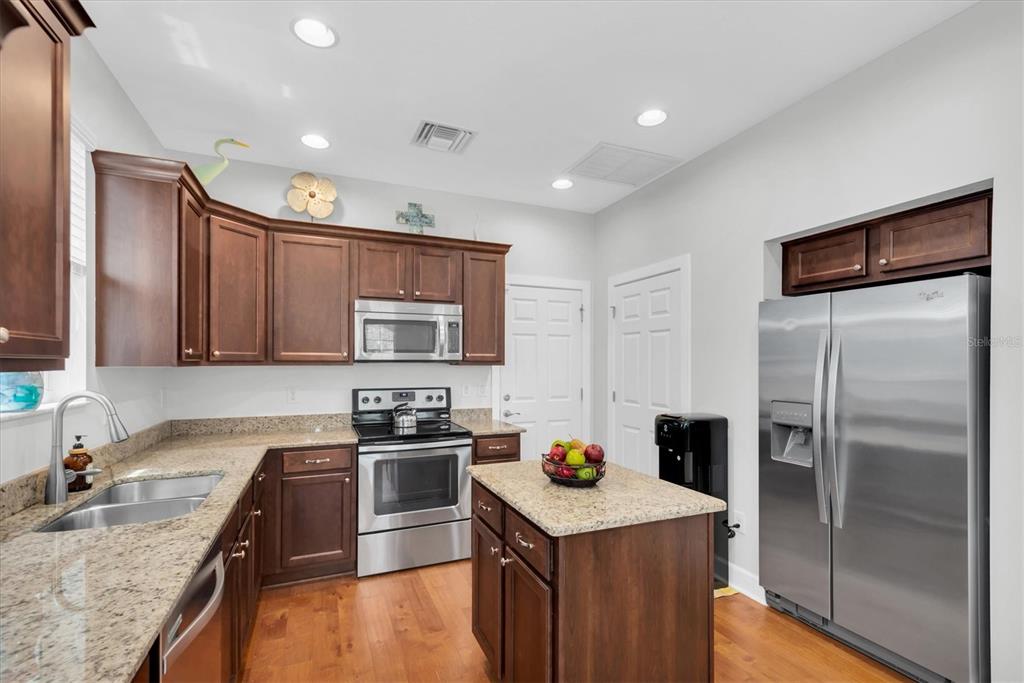 A kitchen features dark wood cabinets, granite countertops, stainless steel appliances, and a center island — 208 CUTLASS WAY, OLDSMAR, FL
