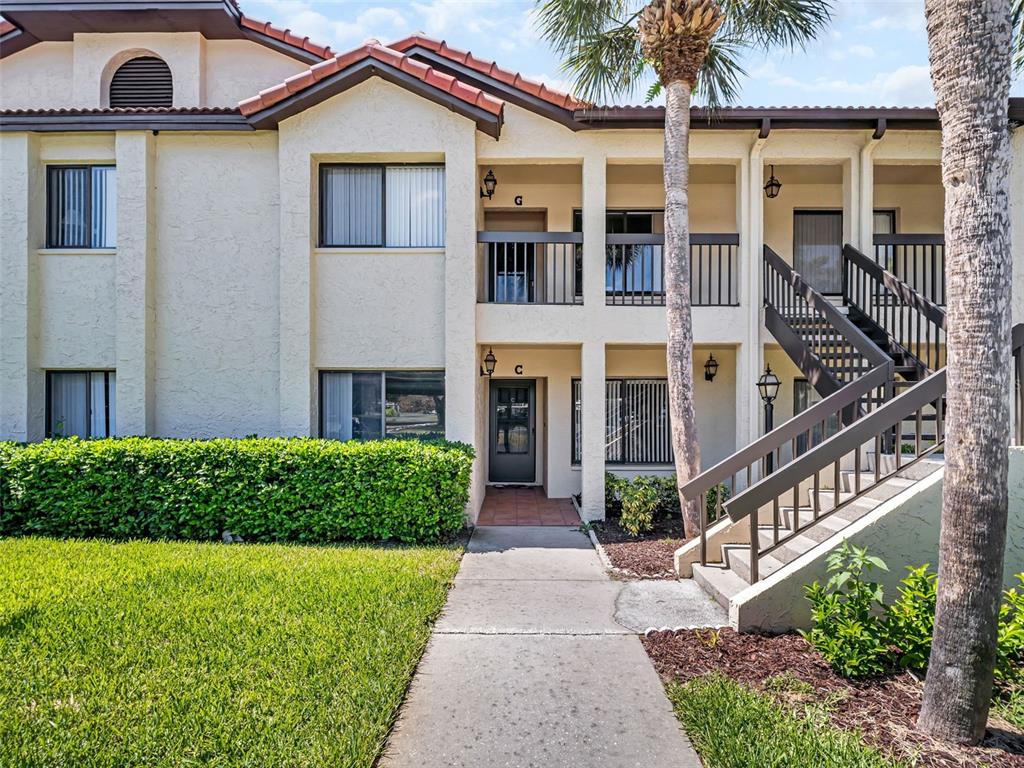 A two-story apartment building exterior features a concrete walkway, stairs, and a palm tree — 1801 E LAKE ROAD UNIT 20C, PALM HARBOR, FL