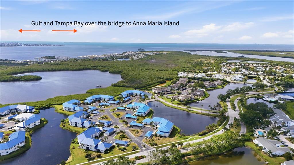 An aerial view shows a residential community with blue-roofed buildings surrounded by water and vegetation — 879 AUDUBON DRIVE UNIT 879, BRADENTON, FL