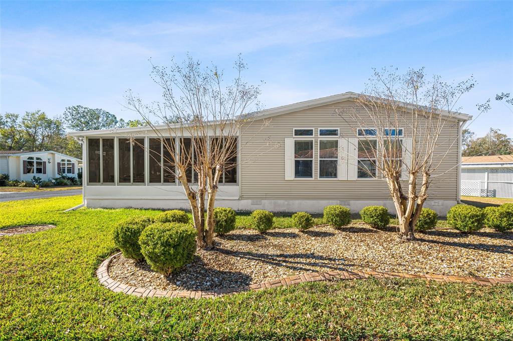 A single-story manufactured home with beige siding, a screened-in porch, and a landscaped front yard — 2973 KINGSWOOD CIRCLE, BROOKSVILLE, FL