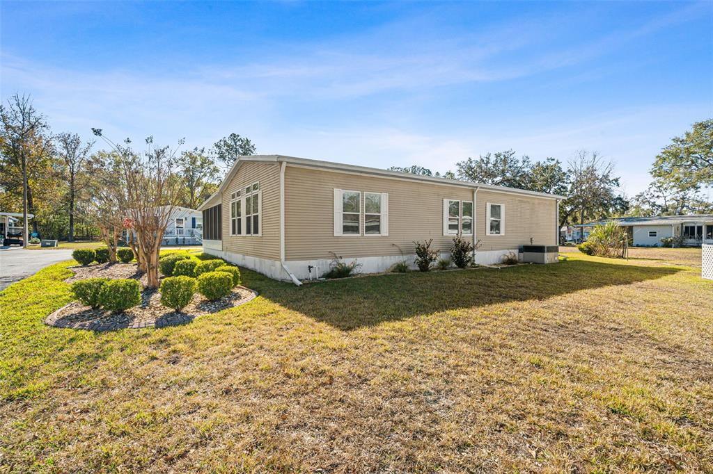 A side view of a tan manufactured home with a landscaped garden and lawn — 2973 KINGSWOOD CIRCLE, BROOKSVILLE, FL