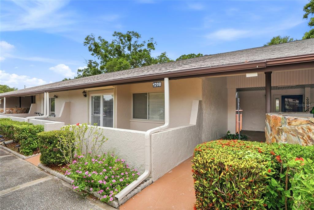 A red front door with a side window sits under a covered entryway with pavers — 1208 14TH CIRCLE SE, LARGO, FL