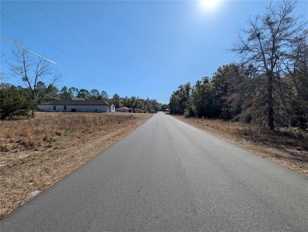 A paved road stretches into the distance between a grassy lot and wooded area — SW SOUNDVIEW DRIVE, DUNNELLON, FL