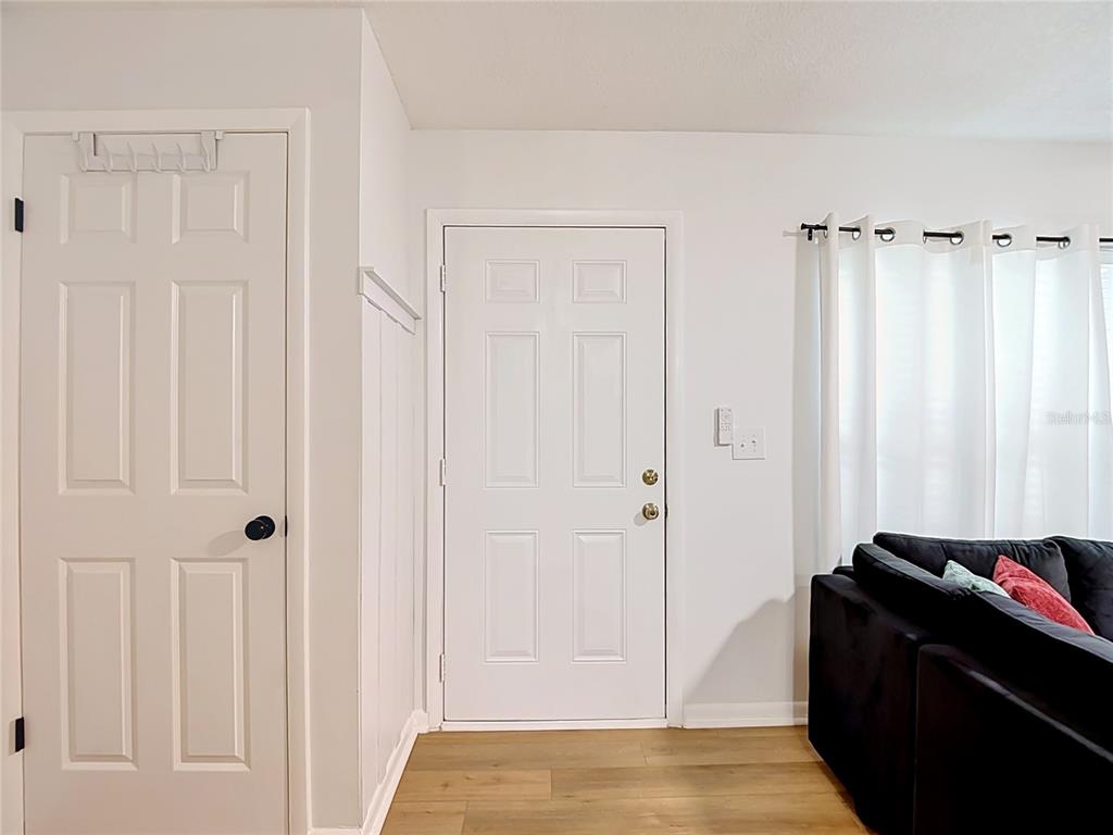 A room with white walls, wood-look flooring, a front door, and a black sofa — 14732 PINE GLEN CIRCLE, LUTZ, FL