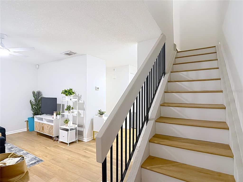 A living room with light wood flooring features a staircase with black metal railings — 14732 PINE GLEN CIRCLE, LUTZ, FL