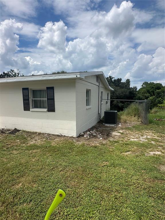 The exterior of a white concrete block house features dark shutters and an air conditioning unit — 651 LORRAINE CIRCLE, LAKE WALES, FL