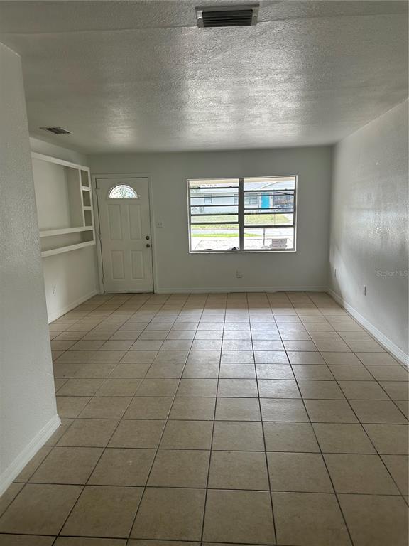 A living room with light-colored tile flooring, white walls, a front door, and a window — 651 LORRAINE CIRCLE, LAKE WALES, FL