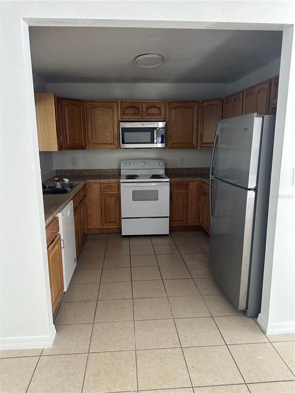 A kitchen features wood cabinets, white appliances, a stainless steel refrigerator, and tiled flooring — 651 LORRAINE CIRCLE, LAKE WALES, FL