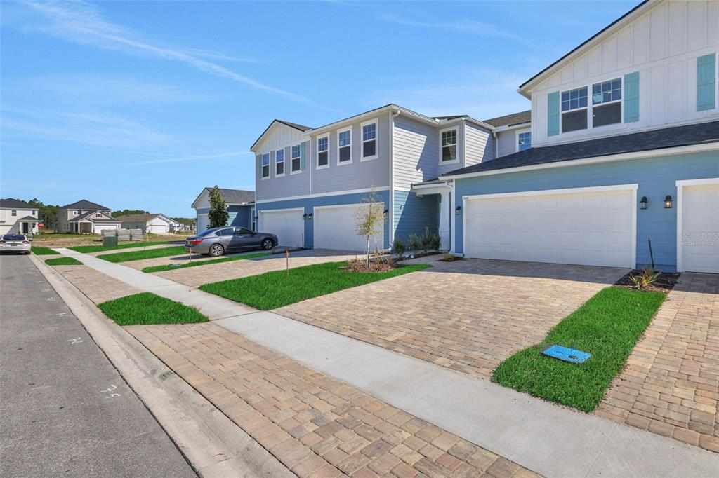 A row of modern two-story townhomes with blue siding and paved driveways under a clear sky — 357 WOODS LANE, ST AUGUSTINE, FL
