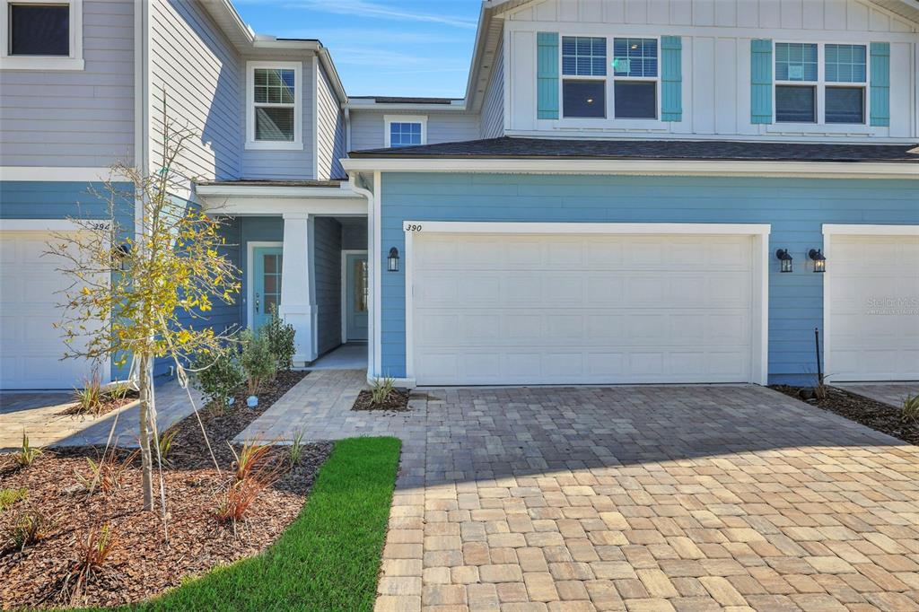 A two-story townhouse exterior features blue siding, a white garage door, and a paver driveway — 357 WOODS LANE, ST AUGUSTINE, FL