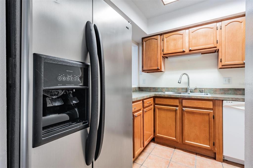 A stainless steel refrigerator stands next to a kitchen with wood cabinets and tile flooring — 2936 LICHEN LANE UNIT B, CLEARWATER, FL