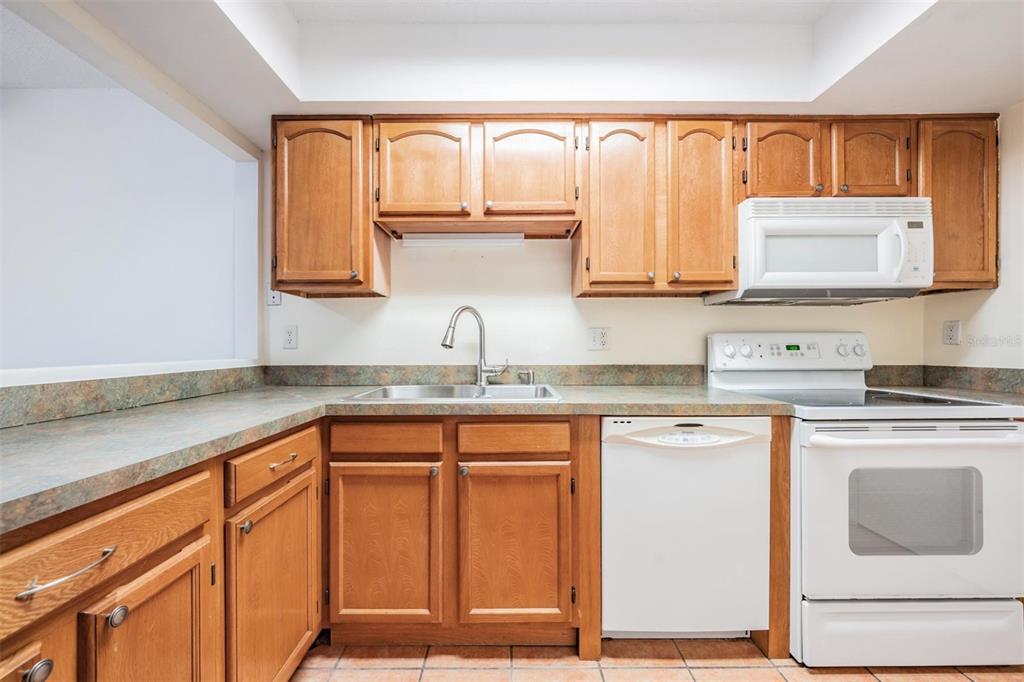 A kitchen features wood cabinets, laminate countertops, a white dishwasher, and a white stove — 2936 LICHEN LANE UNIT B, CLEARWATER, FL