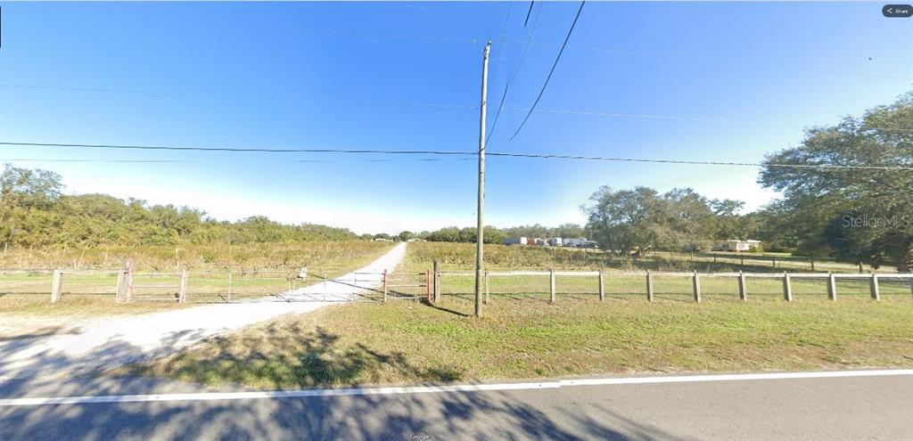 A gravel driveway leads through a metal gate into a large, open, grassy field — GERBER DAIRY RD, WINTER HAVEN, FL