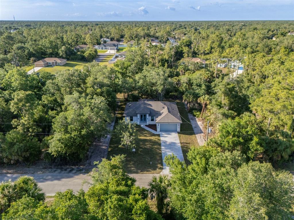 An aerial view shows a single-story house with a driveway surrounded by dense trees — 3466 LANAI, NORTH PORT, FL