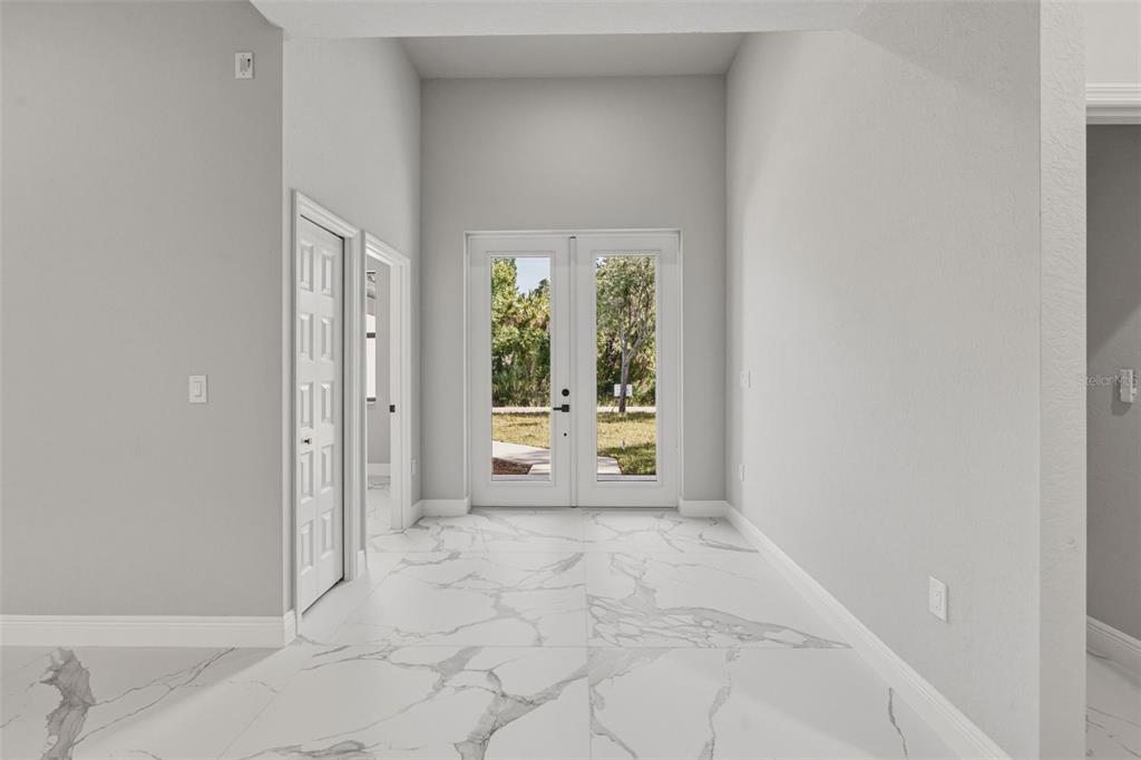 A bright entryway features white marble-look tile flooring, light gray walls, and double glass doors — 3466 LANAI, NORTH PORT, FL