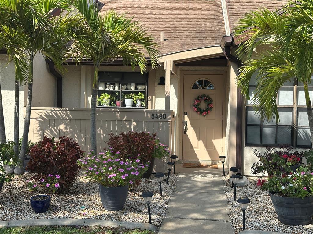 The exterior of a home features a tan front door, palm trees, and potted plants — 5480 BRASSY LOOP, NORTH PORT, FL