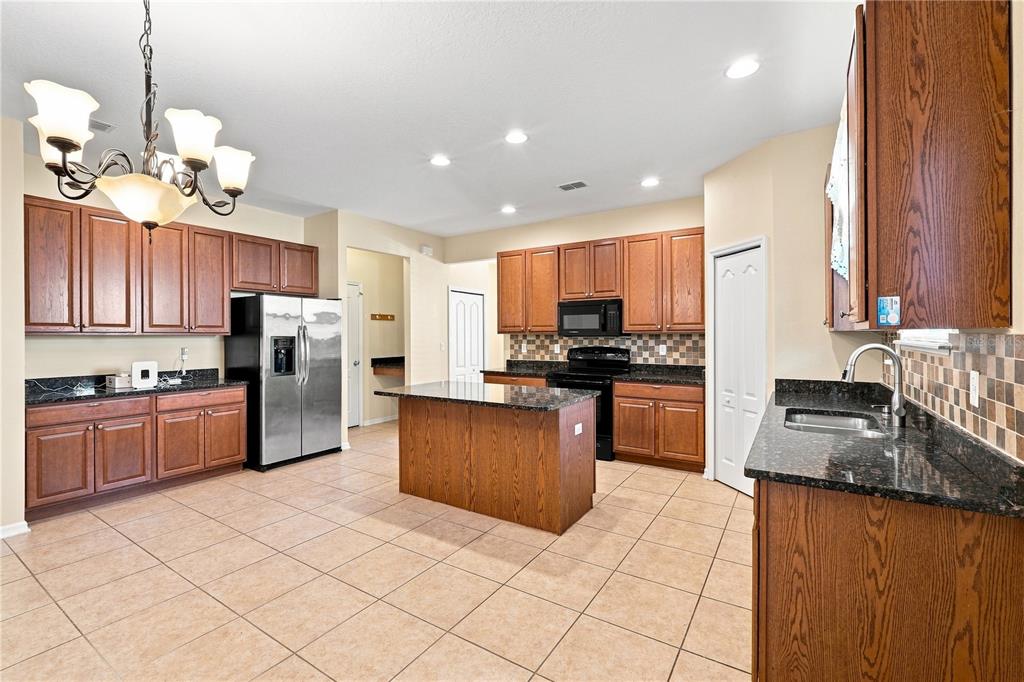A kitchen with wood cabinets, dark granite countertops, a center island, and tile flooring — 2803 MOONSTONE BEND, KISSIMMEE, FL