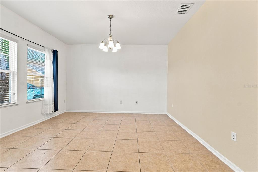 An empty dining room features tile flooring, a chandelier, and two windows with curtains — 2803 MOONSTONE BEND, KISSIMMEE, FL