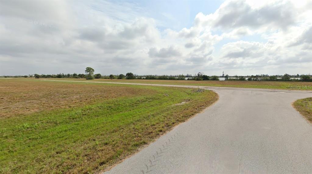 A paved road curves through a large, flat, grassy field under a cloudy sky — 3 PENTAS WAY, PLACIDA, FL