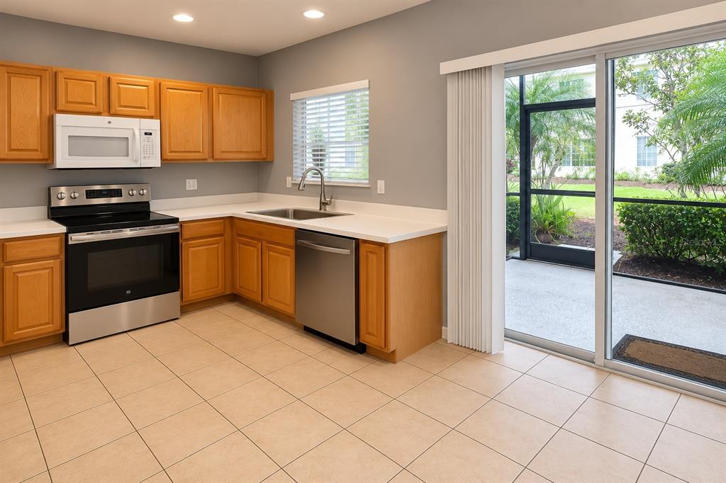 A kitchen with light wood cabinets, stainless steel appliances, tile floors, and a sliding glass door — 215 CAPE HARBOUR LOOP UNIT 103, BRADENTON, FL