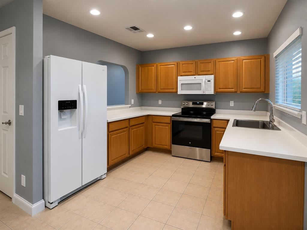 A kitchen features oak cabinets, white countertops, a white refrigerator, and stainless steel appliances — 215 CAPE HARBOUR LOOP UNIT 103, BRADENTON, FL