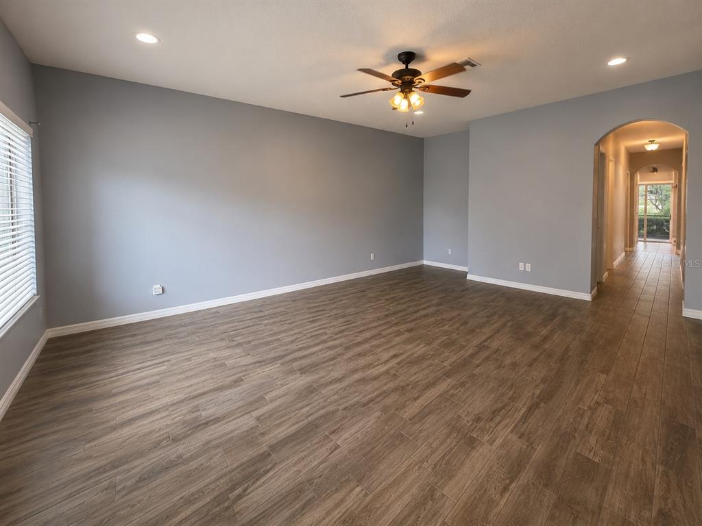 An empty room with gray walls, wood-look flooring, a ceiling fan, and an arched hallway — 215 CAPE HARBOUR LOOP UNIT 103, BRADENTON, FL
