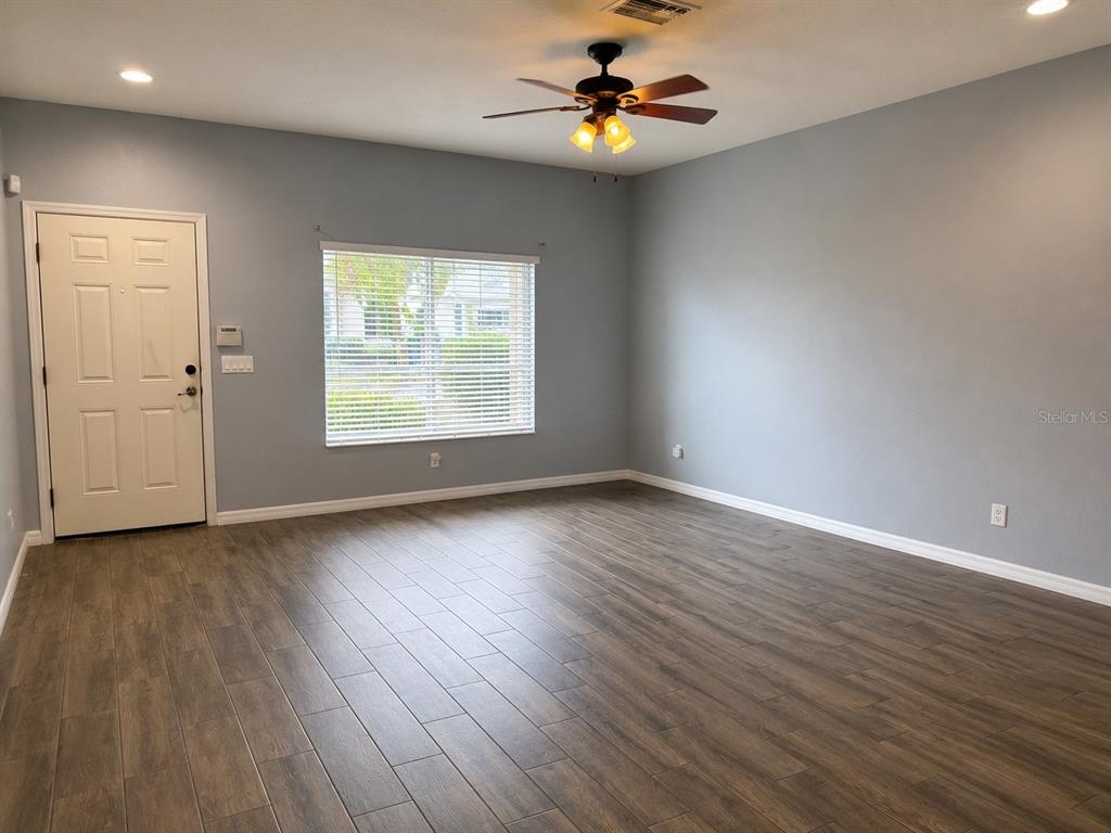 An empty room features light blue walls, wood-look tile flooring, a ceiling fan, and a window — 215 CAPE HARBOUR LOOP UNIT 103, BRADENTON, FL