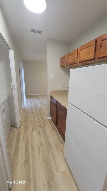 A kitchen features wood cabinets, a white refrigerator, and light-colored wood-look flooring — 4136 PERSHING POINTE PLACE UNIT 5, ORLANDO, FL