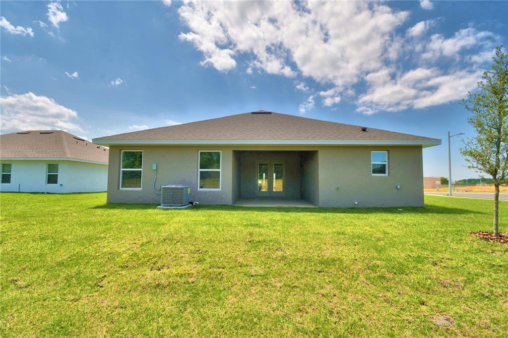 The rear exterior of a single-story house features a covered patio and a grassy yard — 4632 CALAMINT LANE, AUBURNDALE, FL