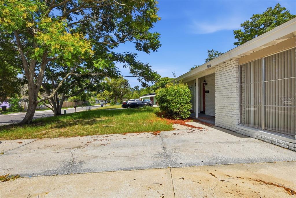 A white brick house exterior features a concrete driveway and a large tree in front — 5312 COVENTRY DRIVE, ORLANDO, FL