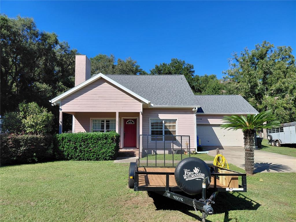 A single-story house with light pink siding, a red front door, and a utility trailer parked — 33 PINE TRACE COURSE, OCALA, FL