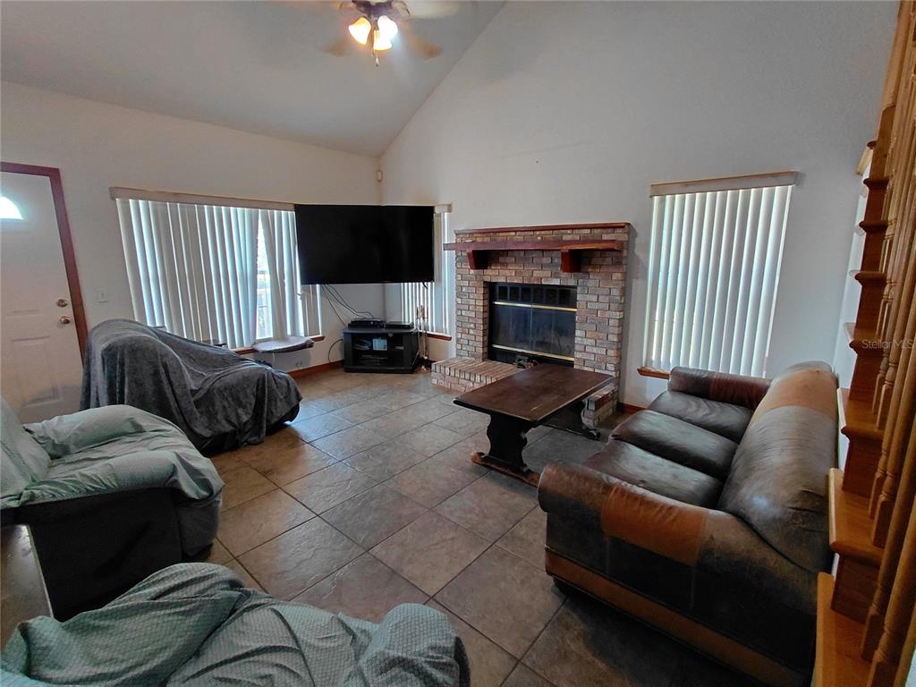 A living room features a brick fireplace, tile flooring, vaulted ceilings, and a large television — 33 PINE TRACE COURSE, OCALA, FL