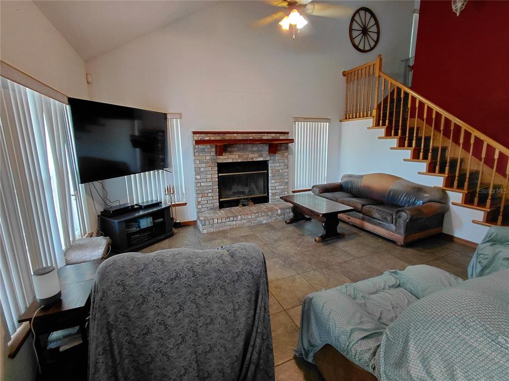 A living room features a brick fireplace, a large television, and a staircase with railings — 33 PINE TRACE COURSE, OCALA, FL
